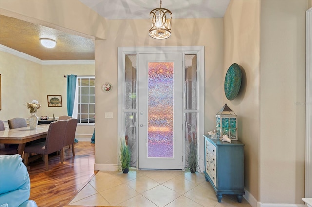 foyer entrance with a textured ceiling, light tile patterned floors, an inviting chandelier, baseboards, and ornamental molding