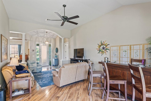 living area featuring lofted ceiling, wood finished floors, arched walkways, decorative columns, and ceiling fan