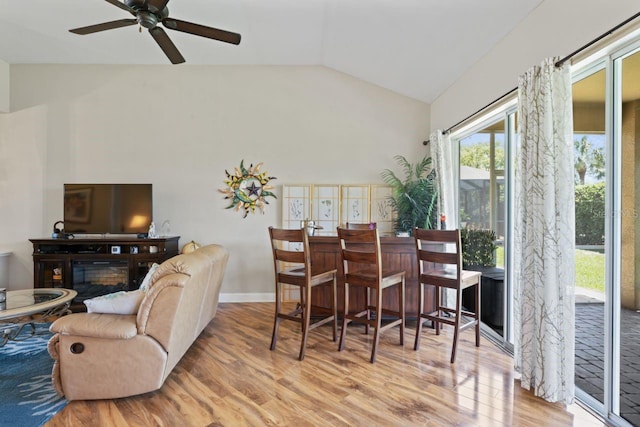 dining room featuring lofted ceiling, a ceiling fan, a glass covered fireplace, and wood finished floors