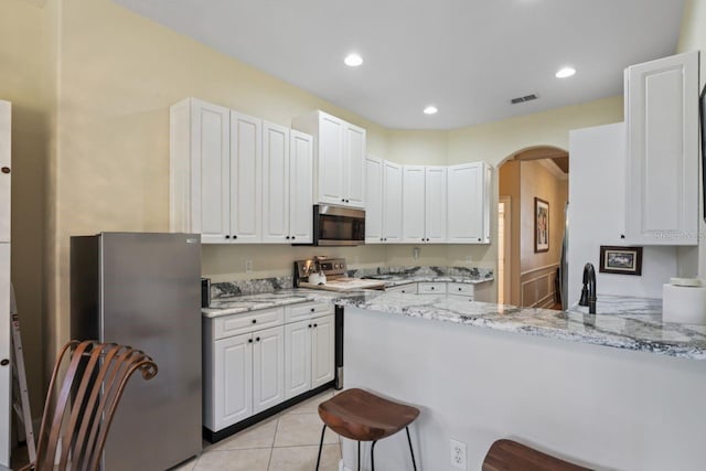kitchen featuring light stone counters, arched walkways, stainless steel appliances, white cabinets, and a peninsula