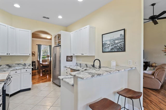 kitchen with a breakfast bar area, arched walkways, a peninsula, light stone countertops, and freestanding refrigerator