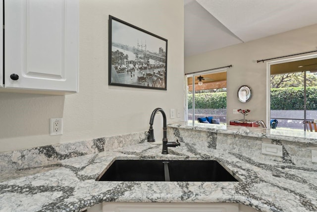 kitchen with light stone countertops, a wealth of natural light, white cabinets, and a sink