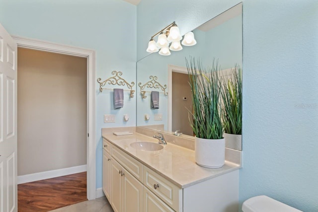 bathroom featuring toilet, baseboards, a notable chandelier, wood finished floors, and vanity