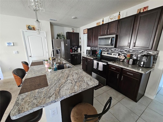 kitchen with a kitchen breakfast bar, a sink, tasteful backsplash, visible vents, and appliances with stainless steel finishes