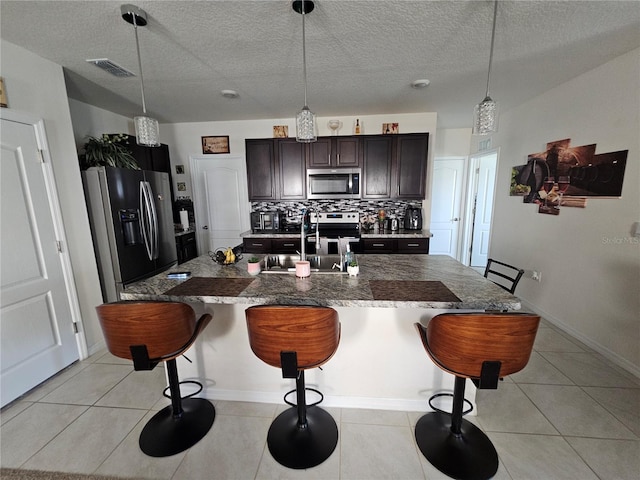kitchen with a sink, visible vents, dark brown cabinetry, appliances with stainless steel finishes, and a breakfast bar area