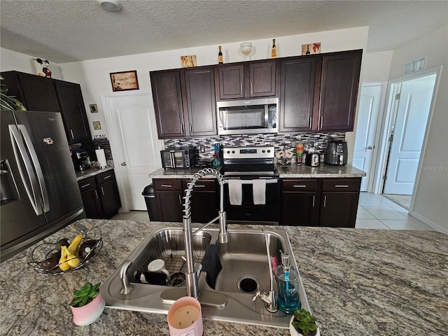 kitchen with dark brown cabinets, visible vents, light tile patterned floors, decorative backsplash, and appliances with stainless steel finishes