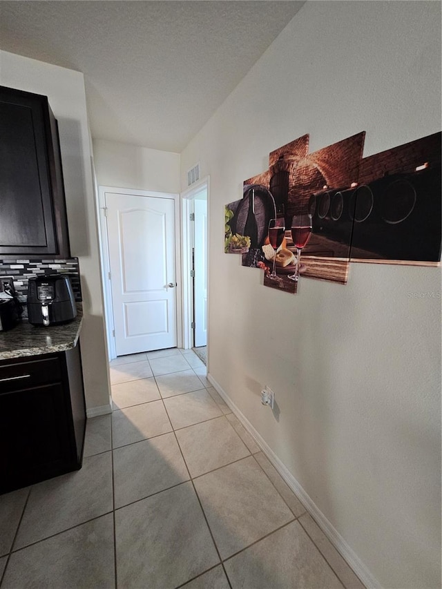 corridor featuring baseboards, visible vents, and light tile patterned floors