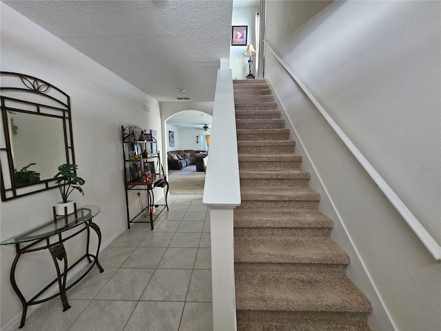 staircase with tile patterned flooring, visible vents, arched walkways, baseboards, and a textured ceiling