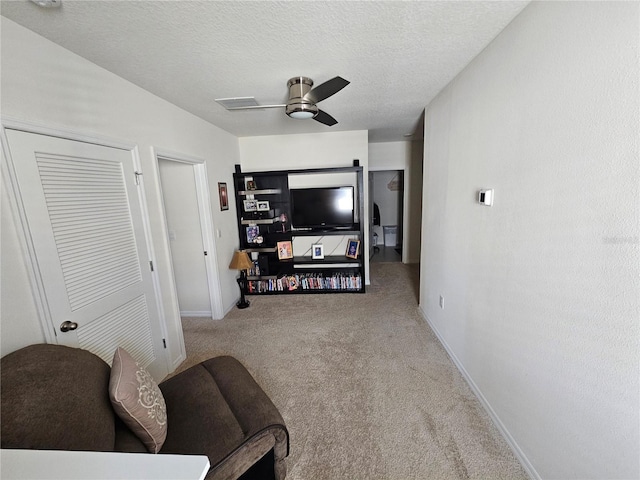 living area featuring baseboards, carpet, a textured ceiling, and ceiling fan