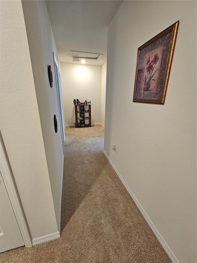hallway with attic access, carpet, and baseboards