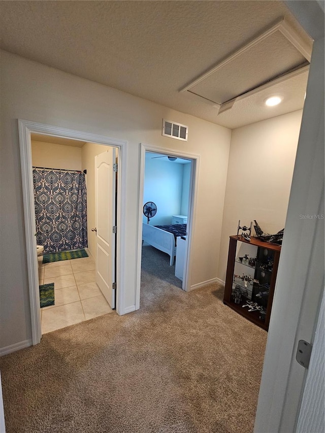 hall with light colored carpet, baseboards, a textured ceiling, and visible vents