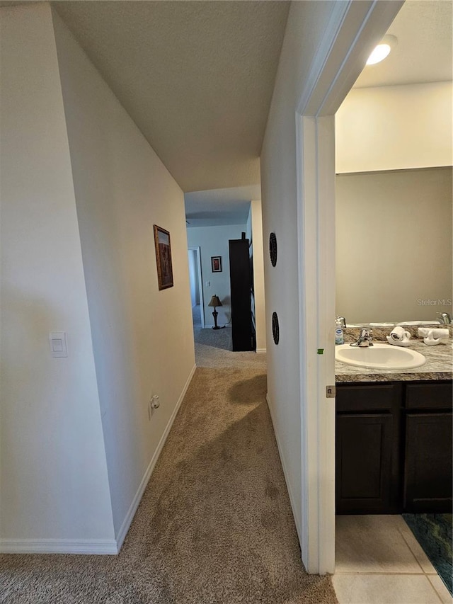 corridor featuring light carpet, baseboards, and a sink