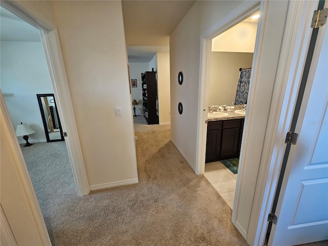 hall with baseboards, light carpet, and a sink