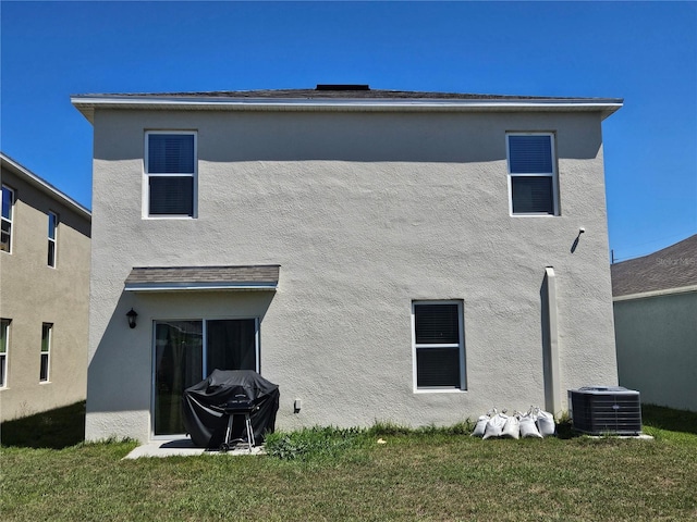 rear view of house with stucco siding, central AC unit, and a lawn