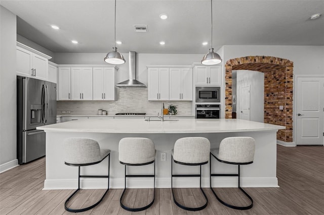 15329 Renaissance Ave, Odessa, FL 33556 - kitchen with stainless steel appliances, light wood-style flooring, a kitchen breakfast bar, and wall chimney range hood