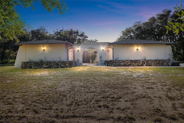 view of front of house with stone siding, a lawn, and stucco siding