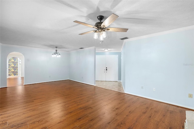 spare room with crown molding, wood finished floors, ceiling fan with notable chandelier, arched walkways, and visible vents