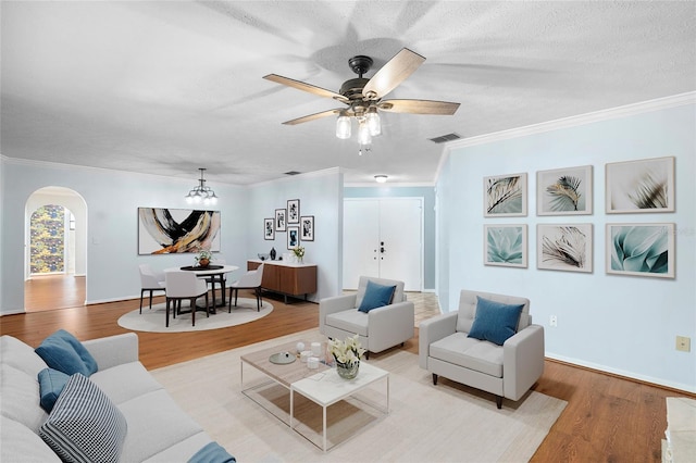 living room featuring crown molding, a ceiling fan, wood finished floors, arched walkways, and visible vents