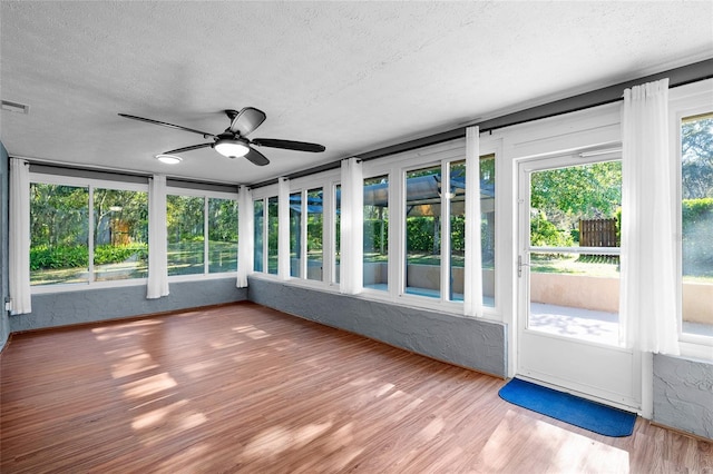 unfurnished sunroom with wood finished floors, a textured ceiling, ceiling fan, and visible vents
