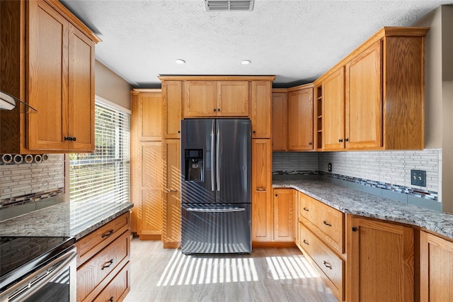 kitchen with light stone counters, tasteful backsplash, stainless steel refrigerator with ice dispenser, visible vents, and recessed lighting