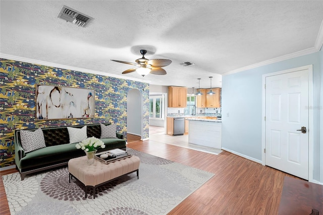 living room with a textured ceiling, light wood-style floors, ceiling fan, ornamental molding, and visible vents