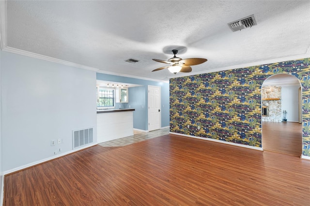 unfurnished living room with a ceiling fan, visible vents, arched walkways, and a textured ceiling