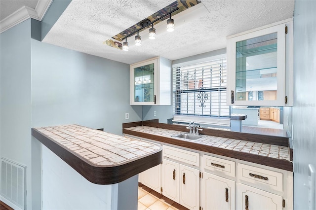 kitchen with tile counters, visible vents, a sink, a textured ceiling, and white cabinetry