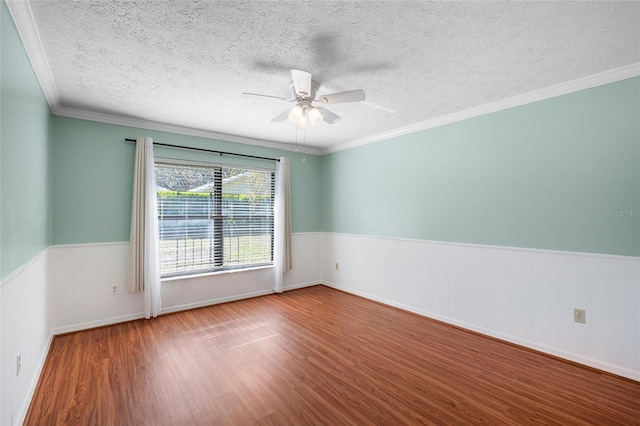 spare room with a textured ceiling, wainscoting, wood finished floors, ceiling fan, and crown molding