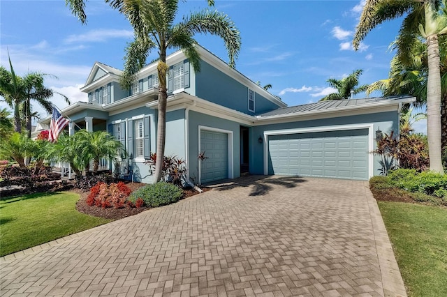 traditional home with decorative driveway, a garage, a front lawn, metal roof, and stucco siding