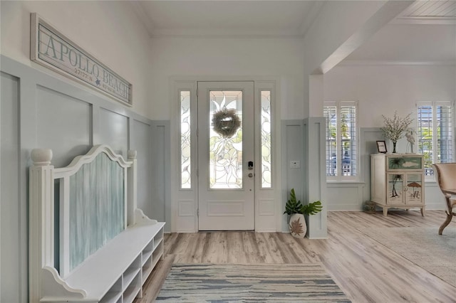 foyer with crown molding, wainscoting, wood finished floors, and a decorative wall