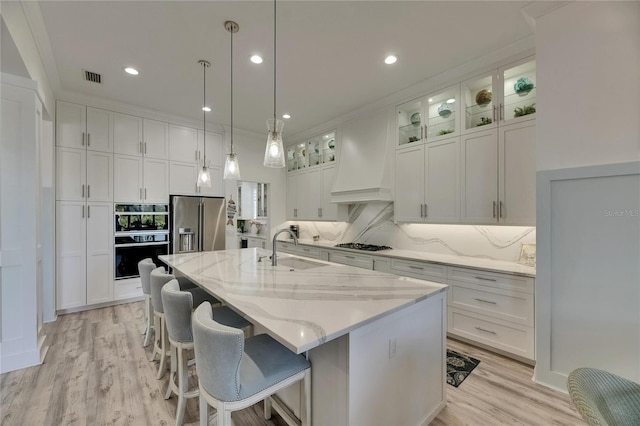 kitchen with a sink, stainless steel appliances, custom range hood, white cabinetry, and visible vents