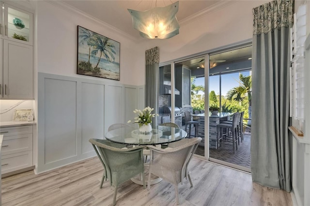 dining area featuring light wood-type flooring, wainscoting, ornamental molding, and a decorative wall