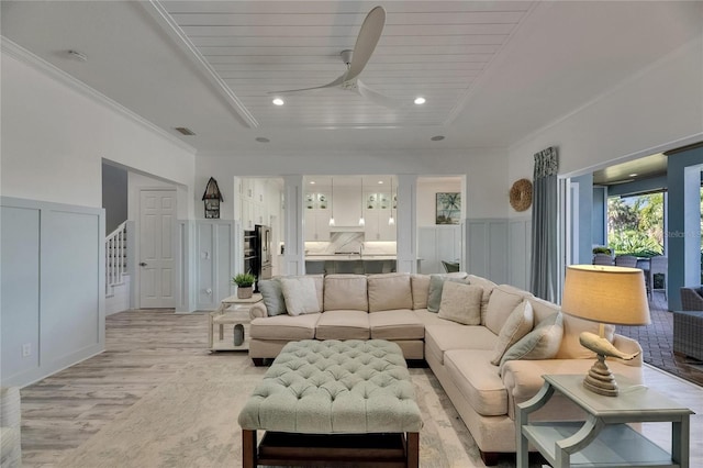 living area with light wood finished floors, a tray ceiling, visible vents, crown molding, and ceiling fan