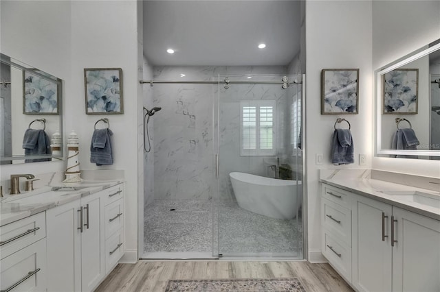 bathroom with two vanities, wood finished floors, a marble finish shower, and a sink