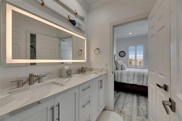 ensuite bathroom with wood finished floors, a sink, double vanity, and crown molding