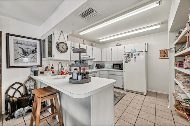 kitchen with light countertops, a peninsula, under cabinet range hood, visible vents, and freestanding refrigerator