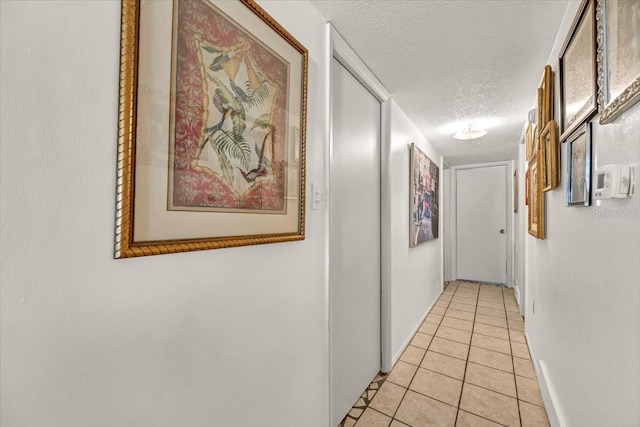 hall featuring baseboards, a textured ceiling, and light tile patterned floors