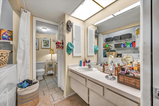 bathroom featuring tile patterned floors, a textured ceiling, vanity, washer and dryer, and toilet