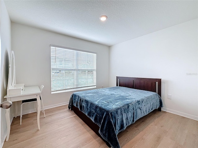 bedroom featuring light wood-style flooring, baseboards, and a textured ceiling