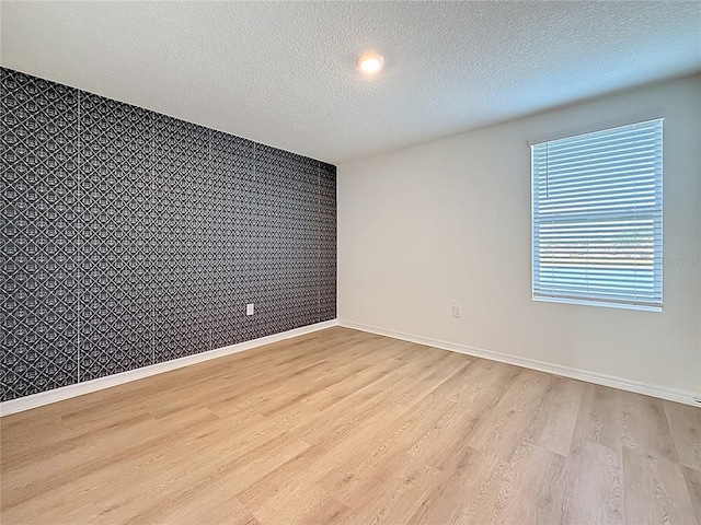 unfurnished room with baseboards, an accent wall, a textured ceiling, and light wood-style flooring