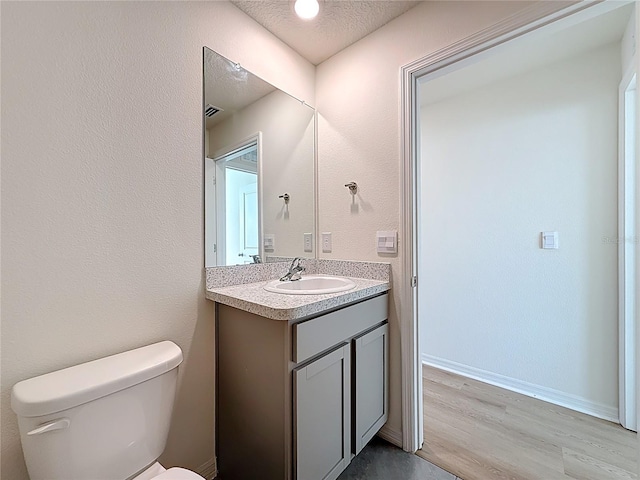 bathroom with wood finished floors, visible vents, toilet, vanity, and a textured ceiling