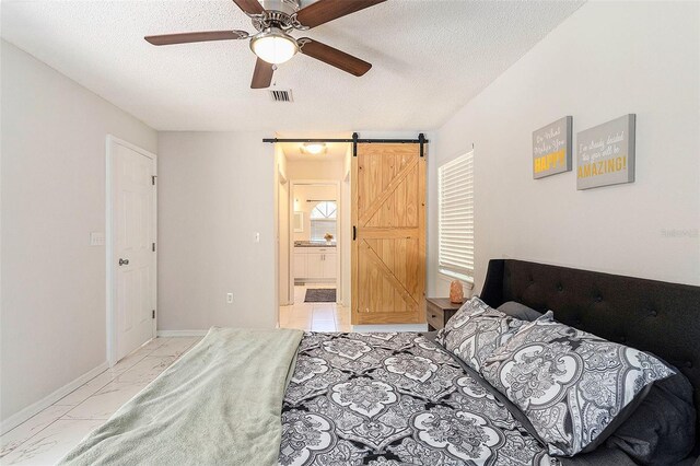bedroom with a barn door, a textured ceiling, ensuite bathroom, marble finish floor, and visible vents