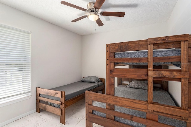 bedroom featuring baseboards, marble finish floor, a textured ceiling, and ceiling fan