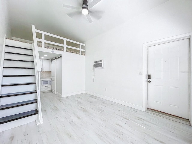 1600 Pasadena Dr, Dunedin, FL 34698 - unfurnished living room with a ceiling fan, a wall mounted AC, light wood-style flooring, and baseboards