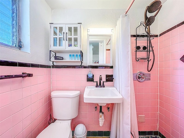 1600 Pasadena Dr, Dunedin, FL 34698 - bathroom featuring a sink, tiled shower, toilet, tile walls, and a wainscoted wall