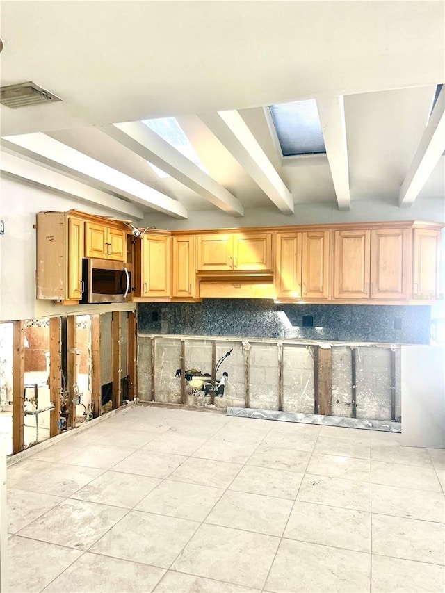 kitchen featuring visible vents, stainless steel microwave, light tile patterned flooring, beam ceiling, and tasteful backsplash