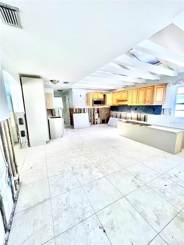 kitchen with light brown cabinets, visible vents, beam ceiling, and stainless steel microwave
