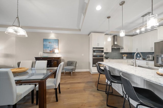 202 Windward Psge Unit 304, Clearwater Beach, FL 33767 - kitchen featuring wall chimney exhaust hood, a tray ceiling, backsplash, wood finished floors, and recessed lighting