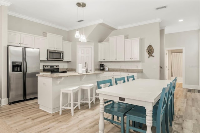 kitchen featuring a kitchen island with sink, light wood finished floors, backsplash, white cabinets, and appliances with stainless steel finishes