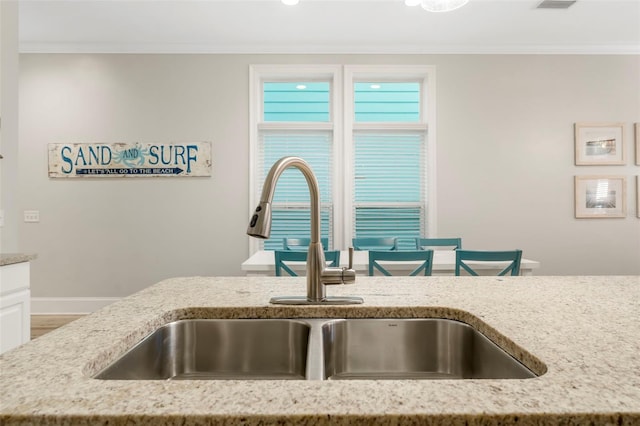 room details with baseboards, light stone countertops, ornamental molding, and a sink